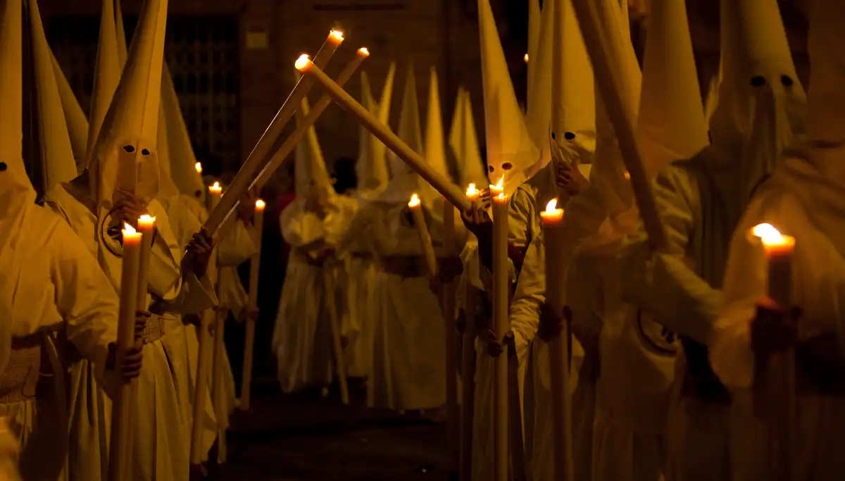 Hooded penitents carrying candles in a Semana Santa procession through Seville