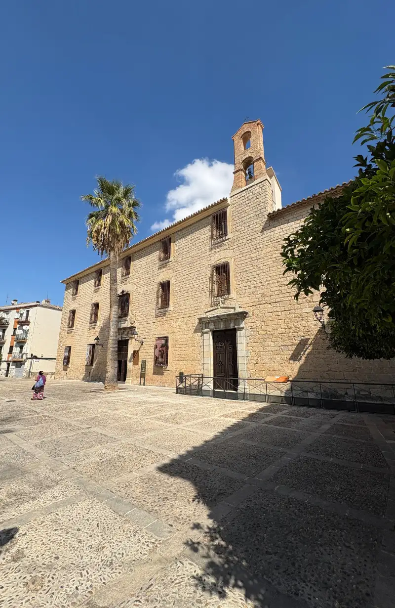 A cobbled plaza in Jaén with a stone church, palm tree and blue sky