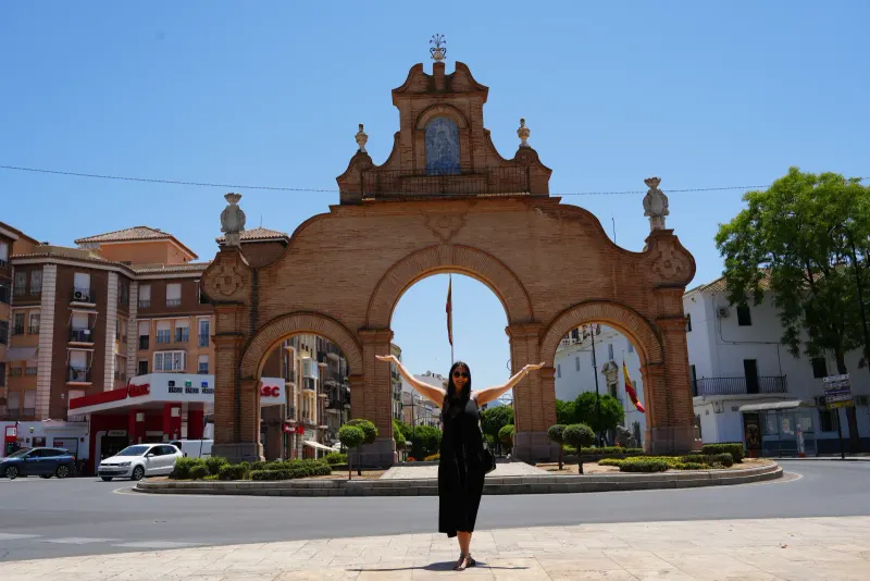 Heidi with arms outstretched in front of the brick Puerta de Estepa gateway in Antequera