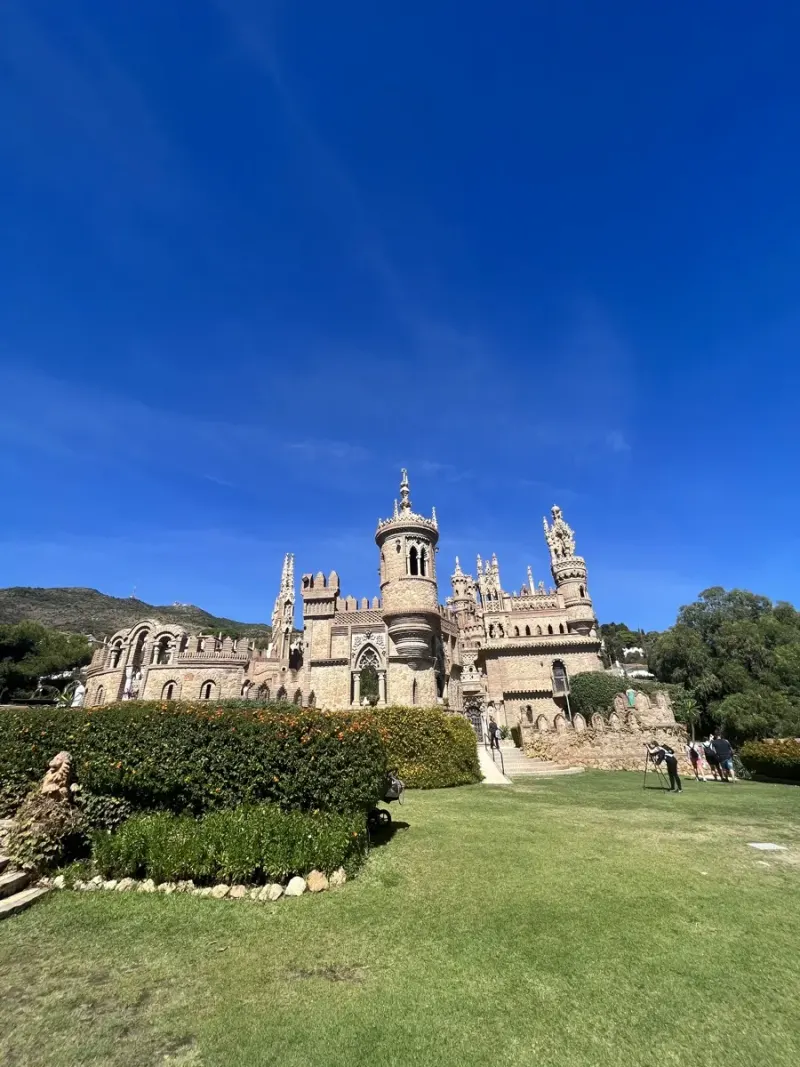 Castillo de Colomares in Benalmádena from the lawn, its stone towers, spires and arches against a deep blue sky, orange-flowered hedges in front