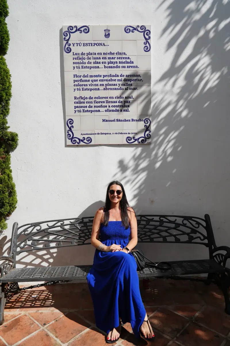Heidi sitting on a wrought-iron bench under a ceramic poem plaque by Manuel Sánchez Bracho in Estepona old town