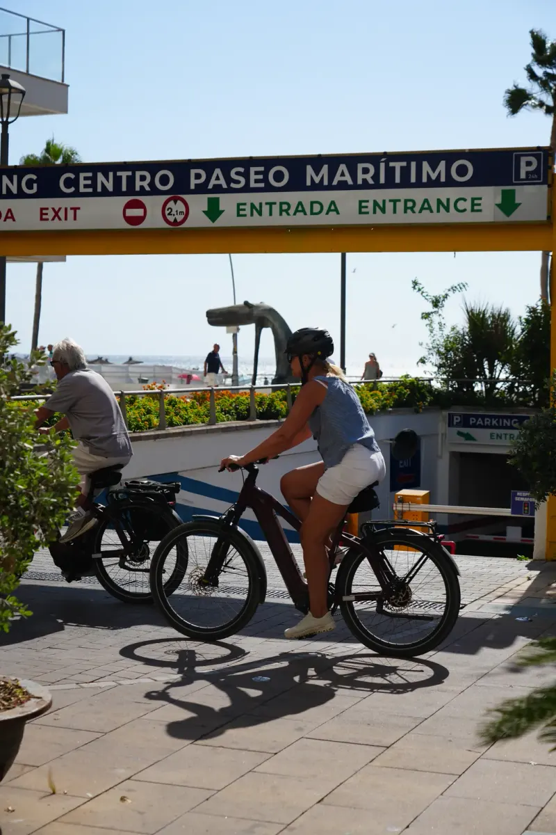 Parking entrance sign for Estepona's Paseo Marítimo car park, with cyclists riding past on the seafront