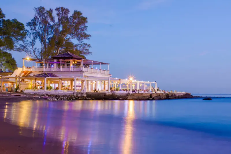 El Balneario's white pavilion on the rocks at Baños del Carmen at dusk, its lights reflected in the water