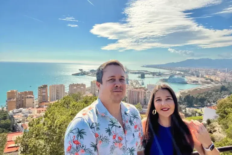 Heidi and Jethro at a Málaga hilltop viewpoint with the port and Mediterranean sea behind them
