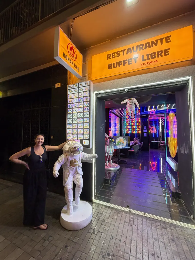 Heidi posing with a life-size astronaut statue outside Konan BBQ, the neon-lit interior visible through the entrance, Málaga