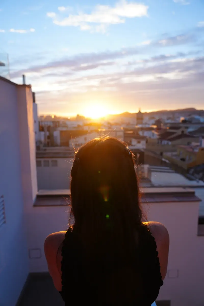 Heidi from behind, silhouetted against the setting sun on the rooftop terrace of Hotel Molina Lario, with Málaga's rooftops spread out below