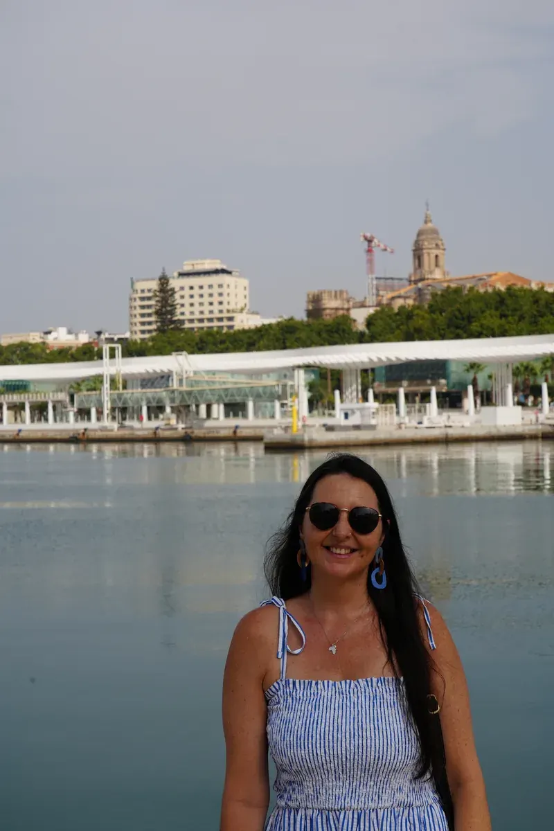 Heidi smiling by the port water in Málaga, with the Cathedral tower behind her