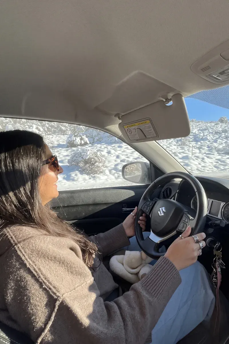 Heidi smiling behind the wheel, driving through the snowy Sierra Nevada