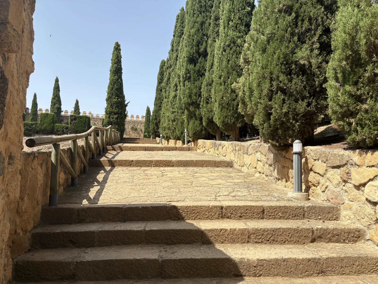 Stone steps climbing a cypress-lined path below the crenellated walls of Antequera's Alcazaba