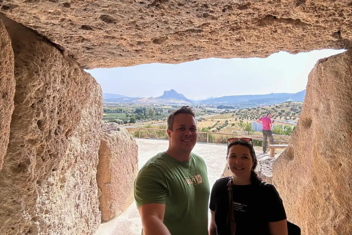Heidi and her husband framed by the stone slabs of a dolmen entrance, with Peña de los Enamorados in the distance near Antequera