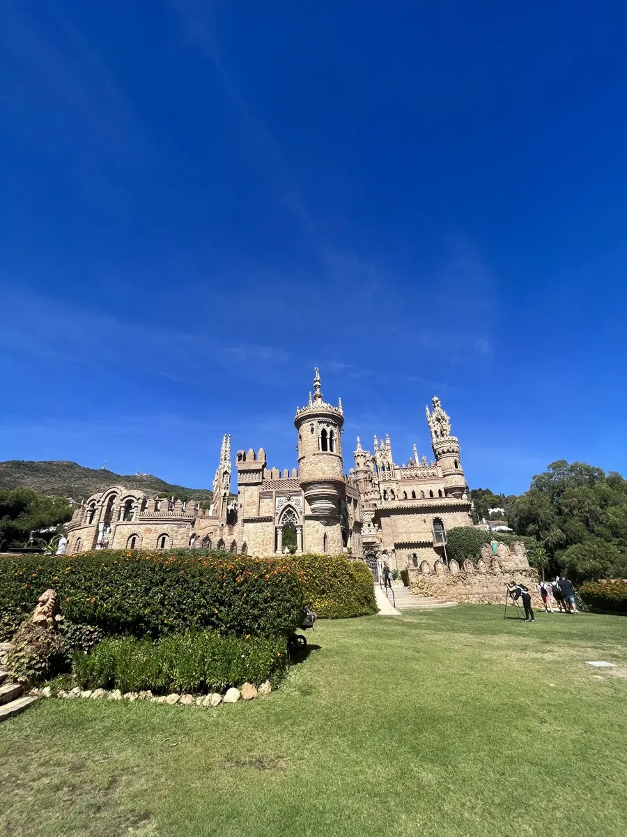 Castillo de Colomares in Benalmádena from the lawn, its stone towers, spires and arches against a deep blue sky, orange-flowered hedges in front