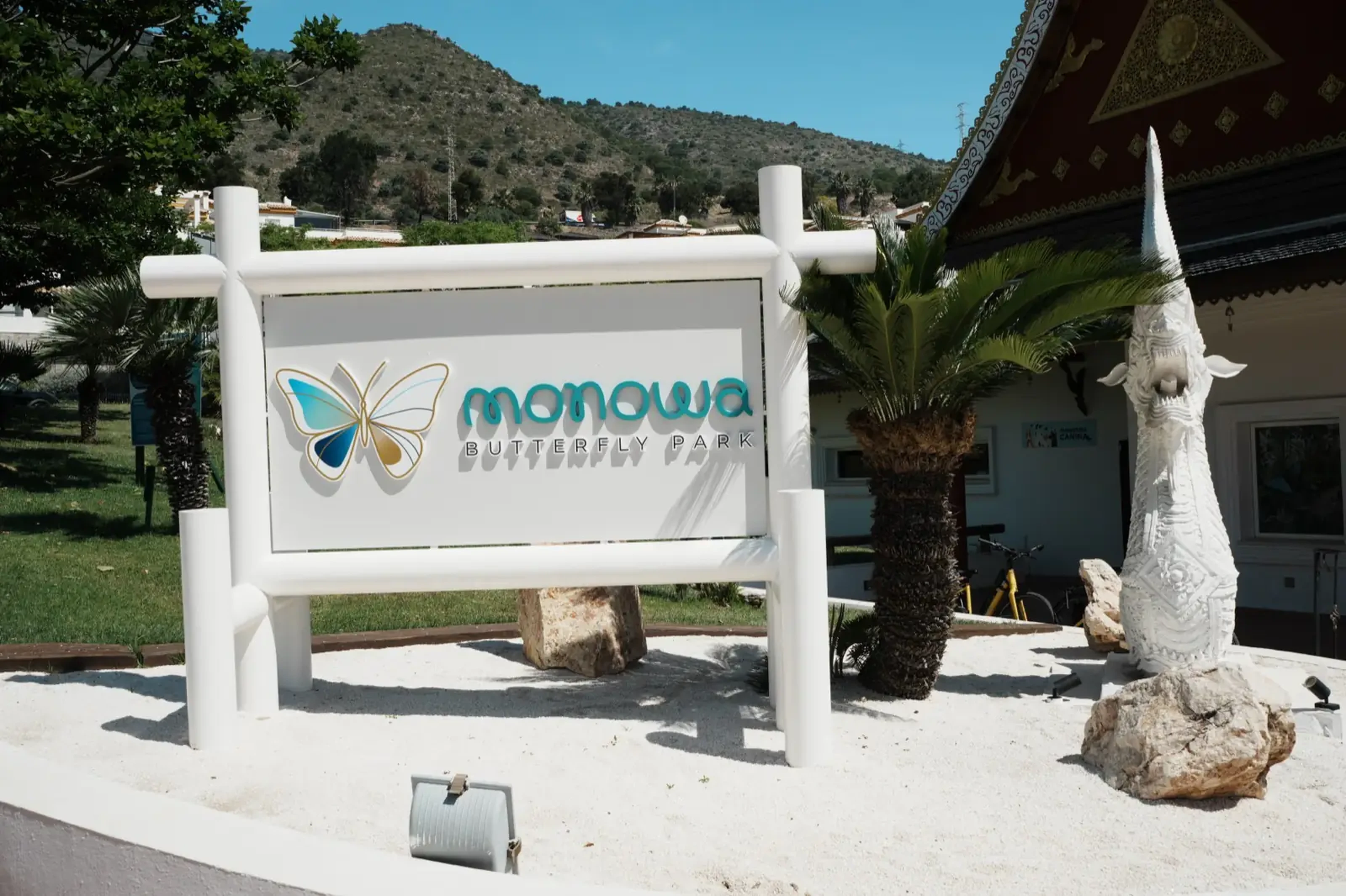 The Monowa Butterfly Park sign in Benalmádena, with a white dragon statue and the Thai-style roof of the butterfly house behind it