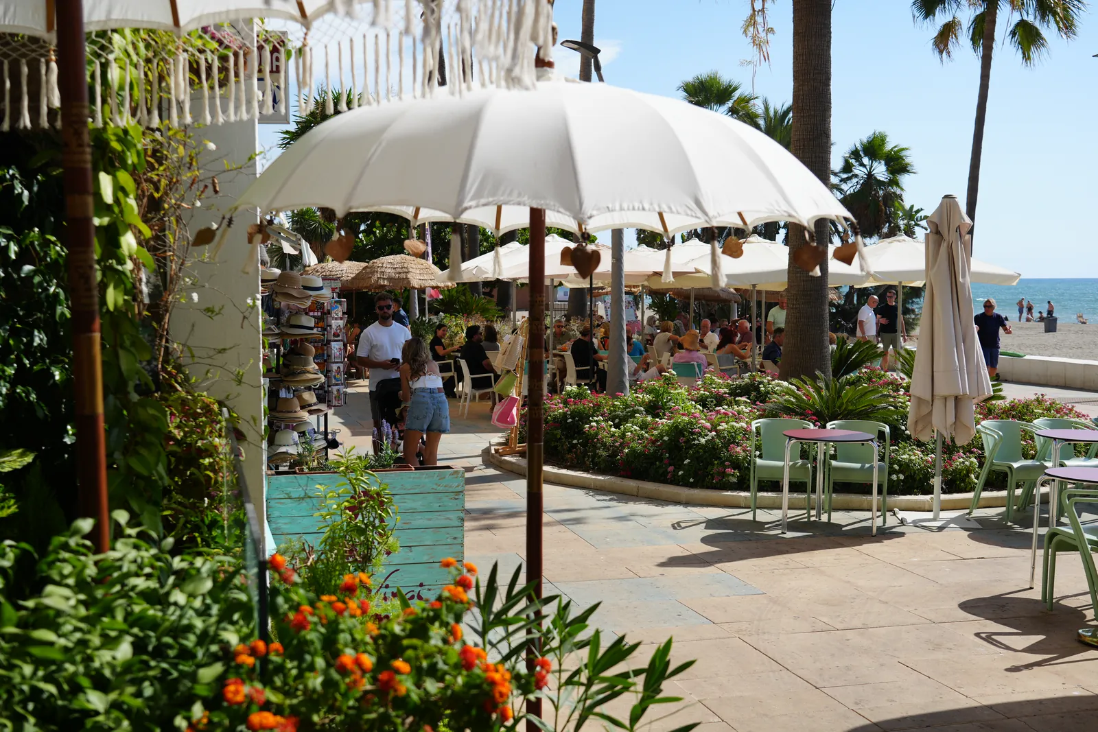 Bali-style umbrellas over a busy beachfront terrace along Estepona's promenade, palm trees and the beach behind