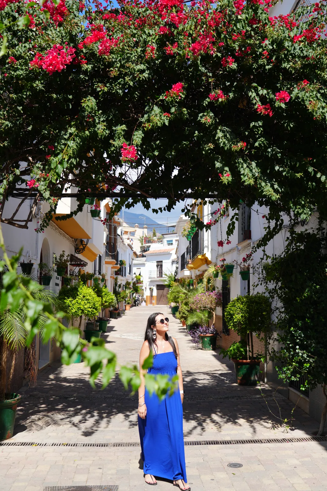 Heidi standing under a bougainvillea-covered canopy on a whitewashed street in Estepona old town