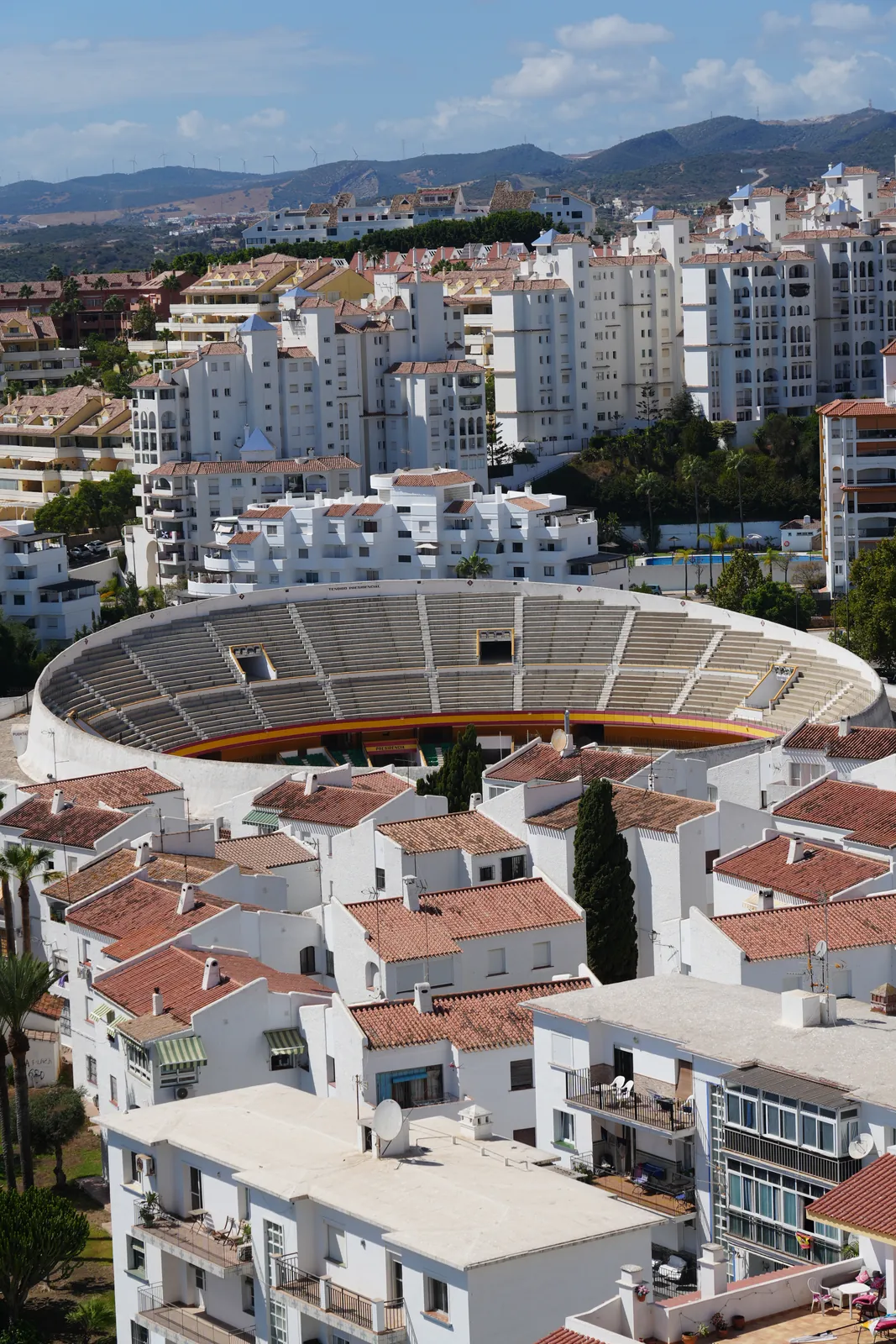 Aerial view of Estepona's round bullring surrounded by whitewashed rooftops, mountains behind