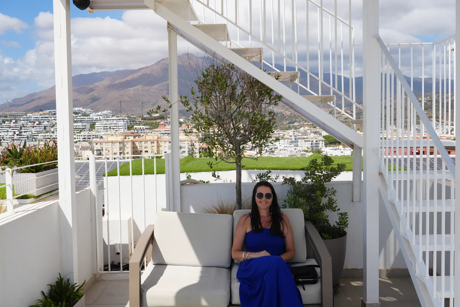 Heidi sitting on a lounge sofa at Cielo rooftop bar in Estepona, with Sierra Bermeja and the town behind her