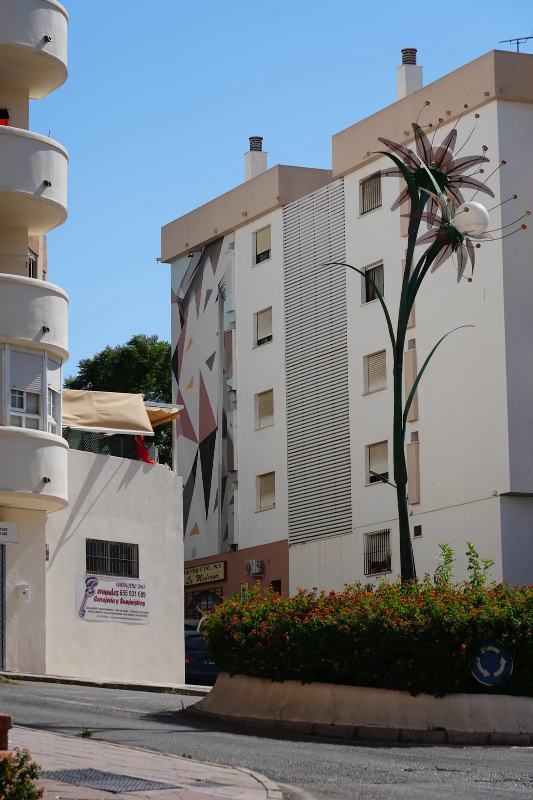 Abstract geometric triangle mural with a metal flower sculpture in front in Estepona