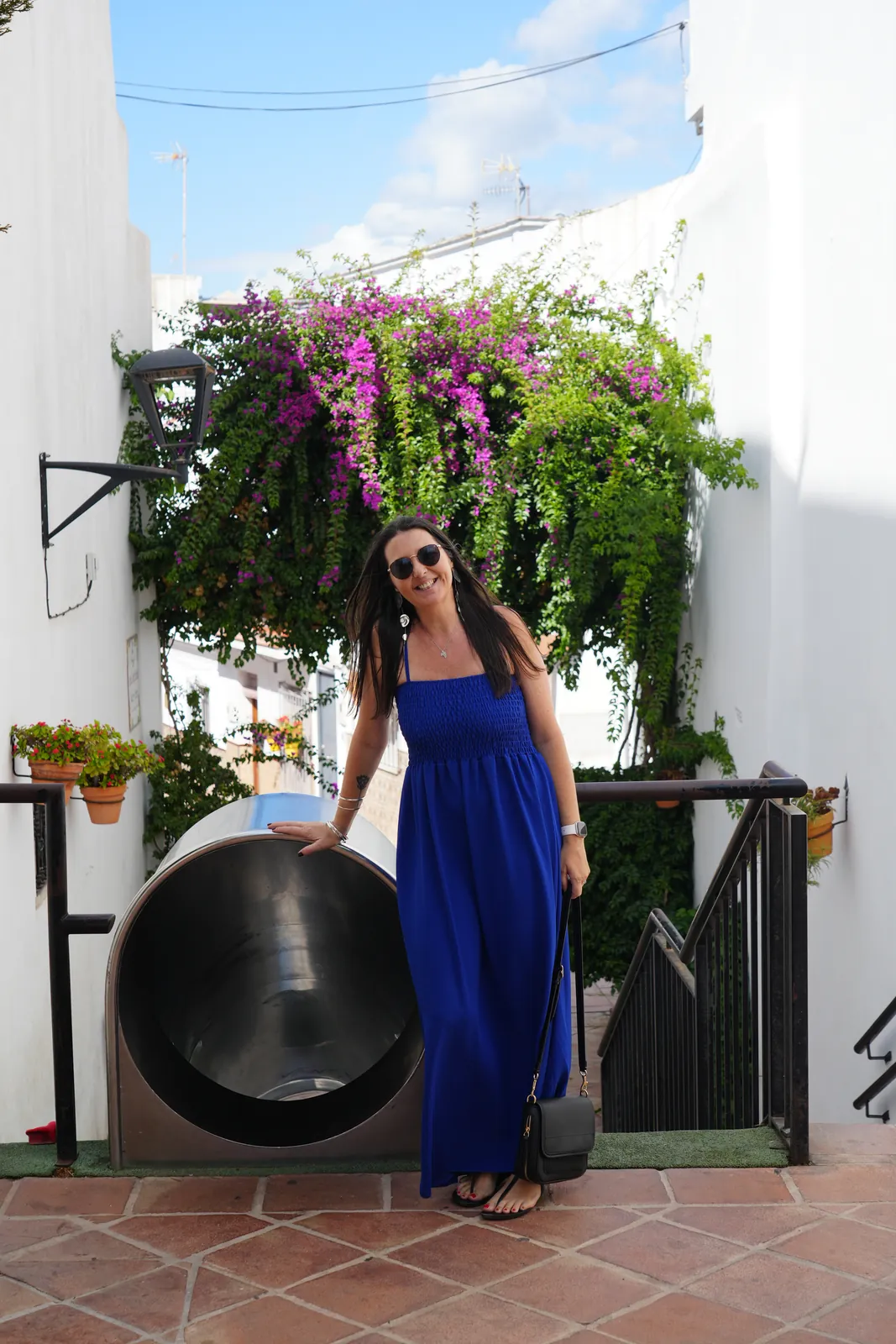 Heidi standing at the mouth of the stainless-steel tube slide in Pasaje Manuel Sánchez Bracho, Estepona old town, bougainvillea hanging overhead