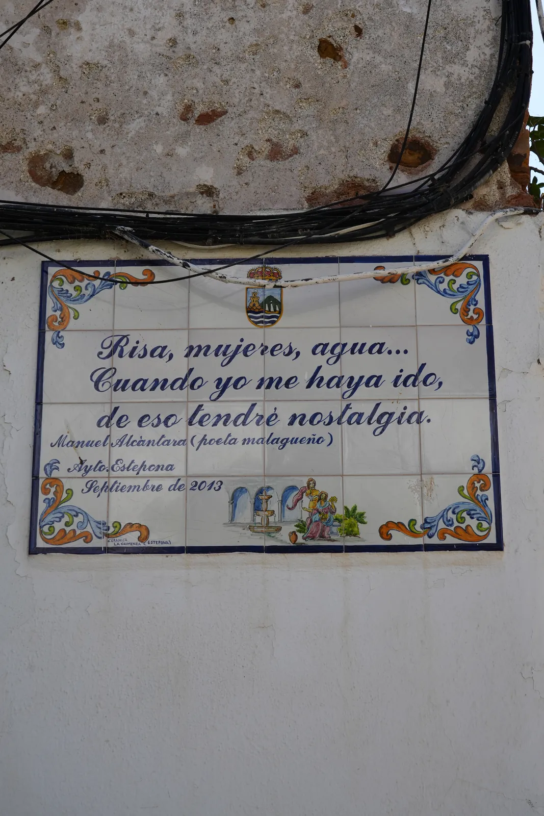 Close-up of Manuel Alcántara's ceramic poem plaque on a weathered wall in Estepona, with exposed cables above it