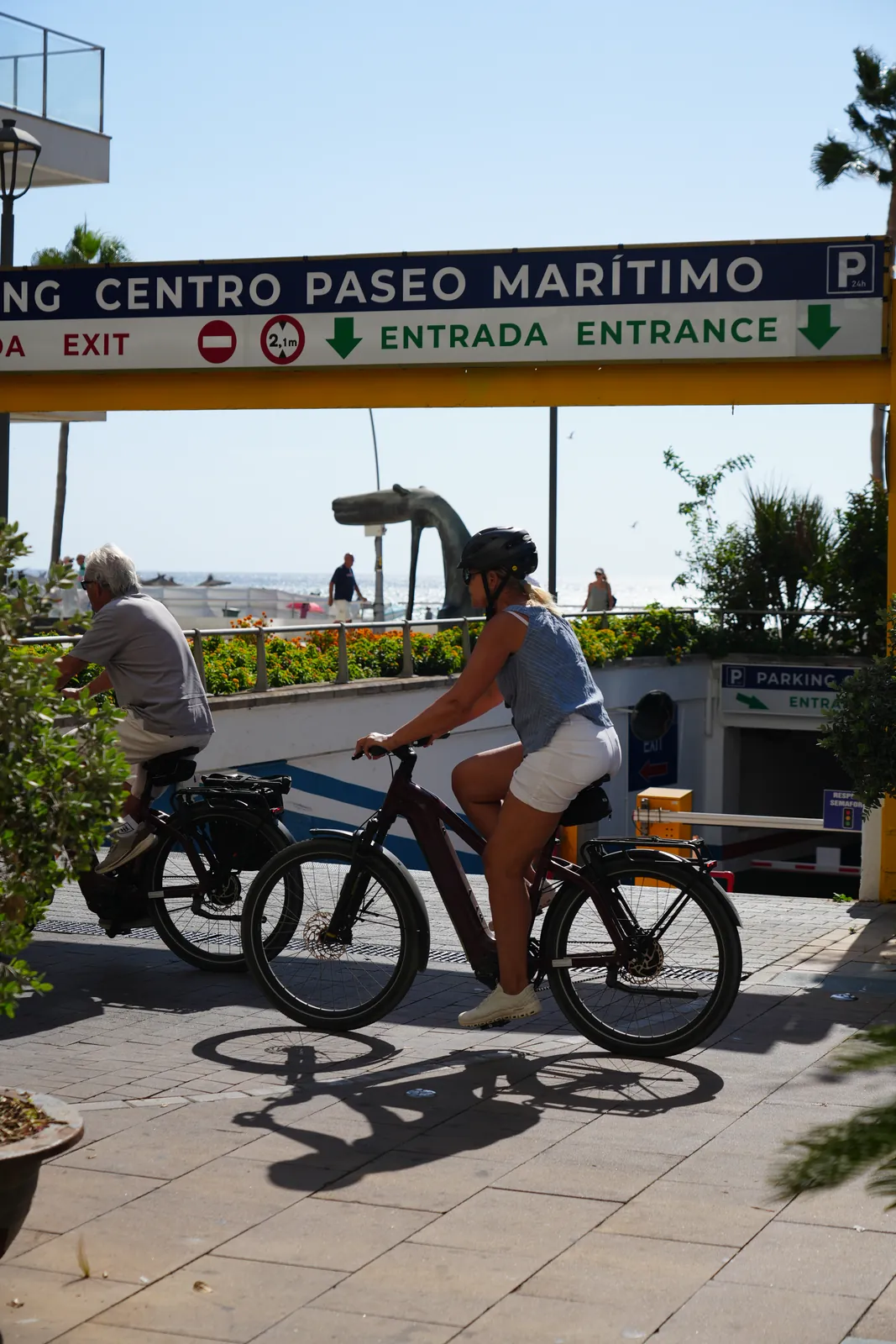 Parking entrance sign for Estepona's Paseo Marítimo car park, with cyclists riding past on the seafront