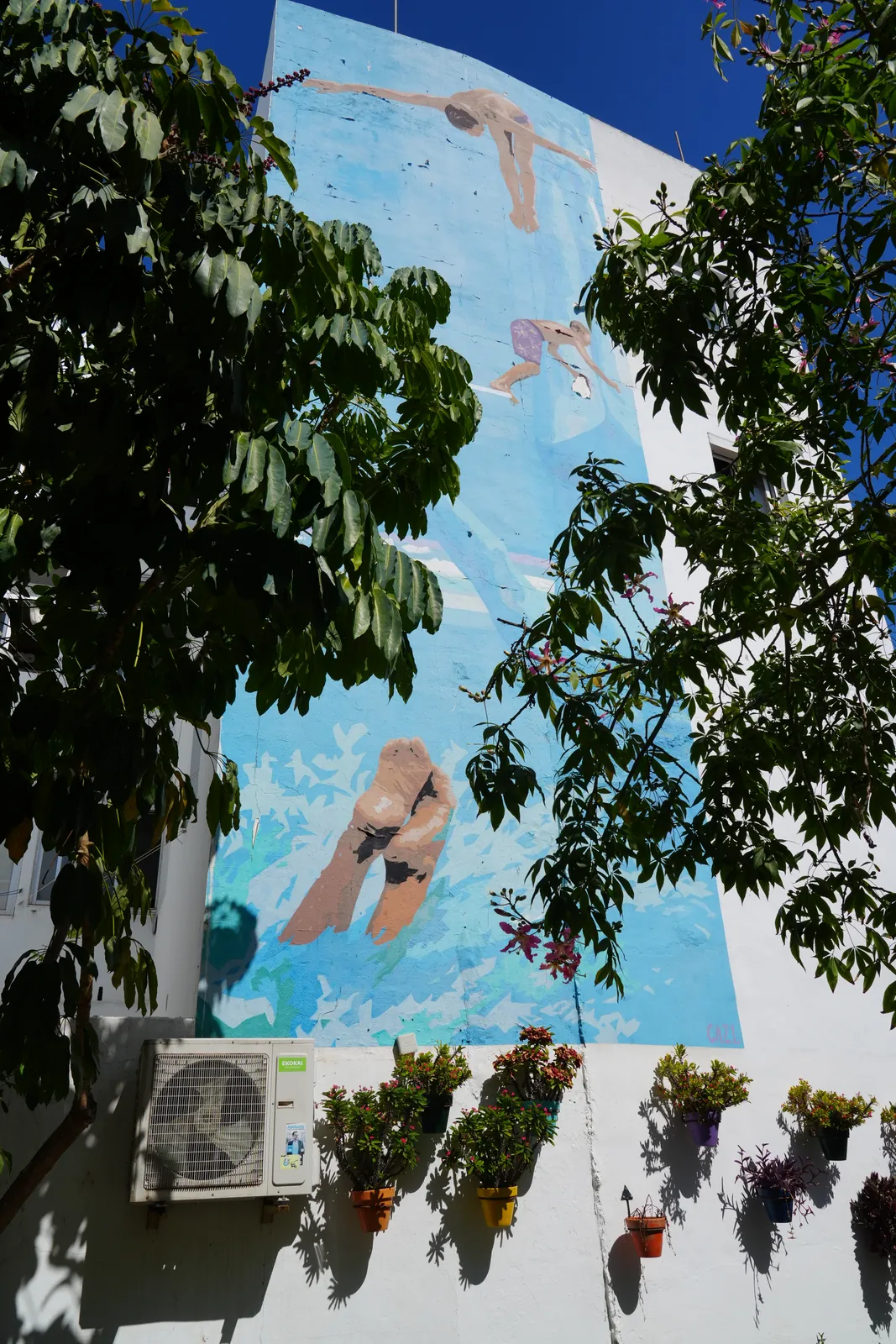 Three swimmers mural against a flat blue wall in Estepona