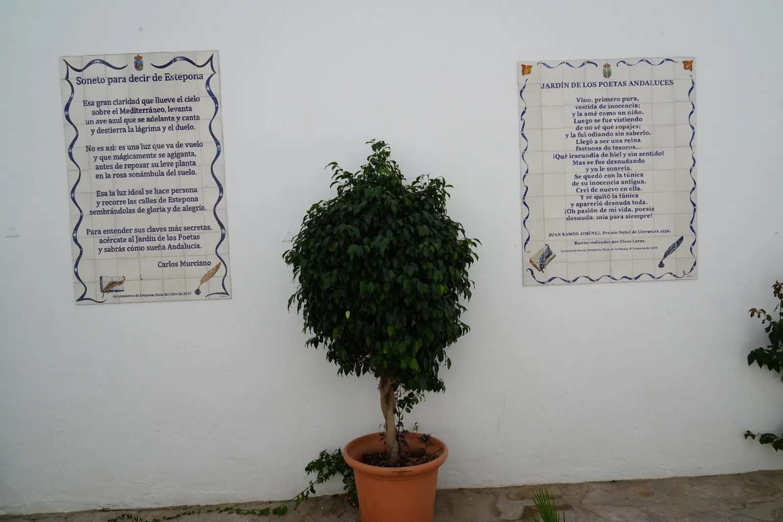 Two ceramic poem plaques side by side in the Jardín de los Poetas Andaluces, one by Carlos Murciano and one by Juan Ramón Jiménez, with a potted tree between them
