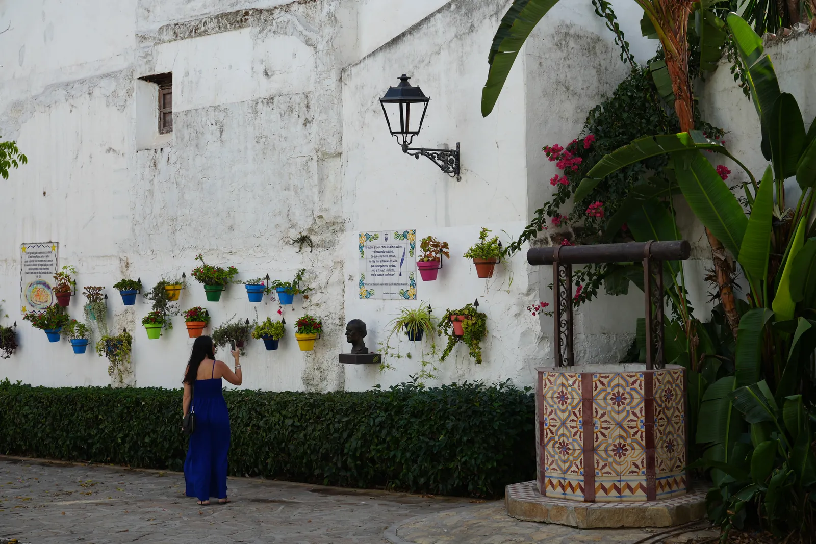 Heidi photographing the colourful hanging flowerpots and tiled well in the Jardín de los Poetas Andaluces, Estepona