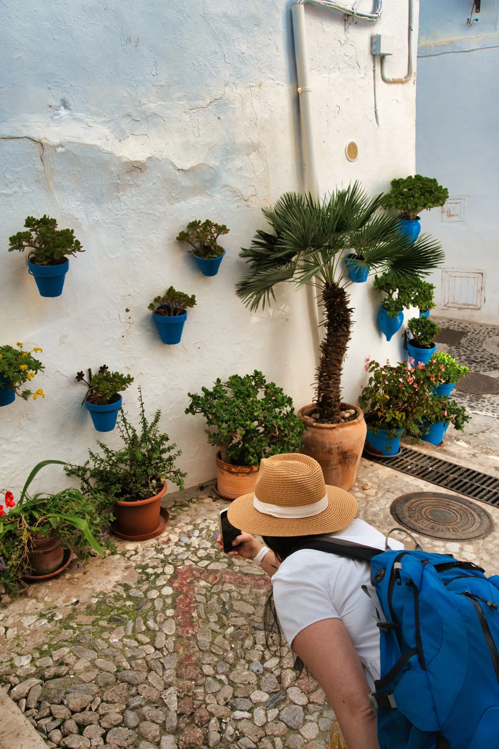 Heidi in a straw hat photographing blue flowerpots on a whitewashed wall in Frigiliana