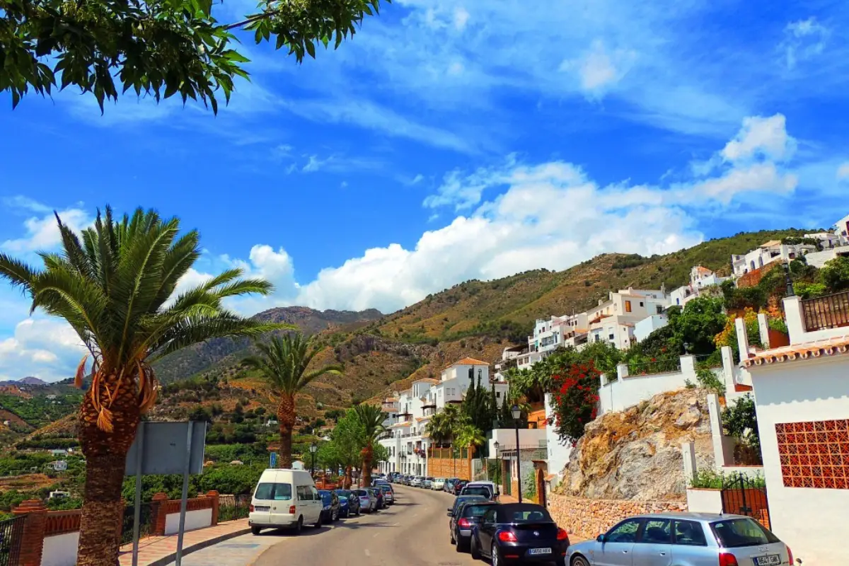 Cars parked on the road into Frigiliana with the white hilltop village behind