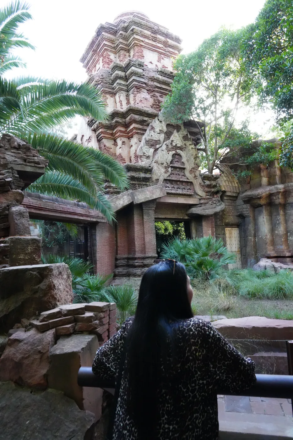 Heidi from behind at a railing, looking toward a tiered stone temple tower and palms at Bioparc Fuengirola