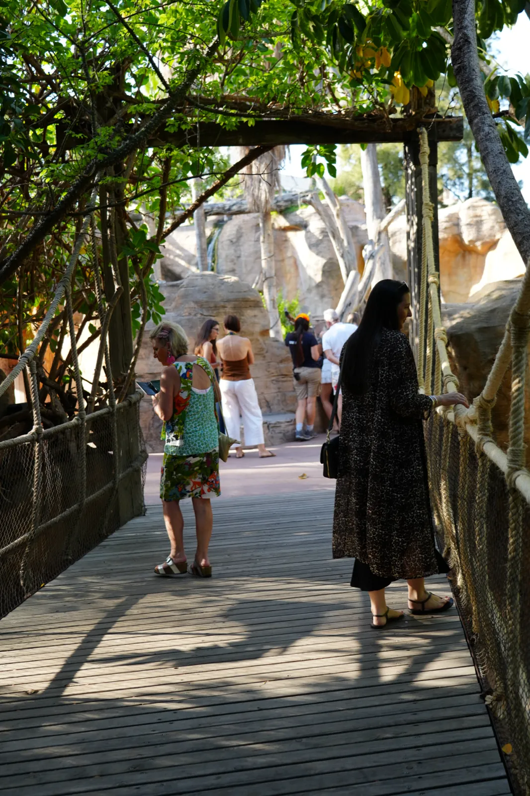 Heidi in a leopard-print cardigan at the rope rail of a wooden boardwalk under the trees at Bioparc Fuengirola
