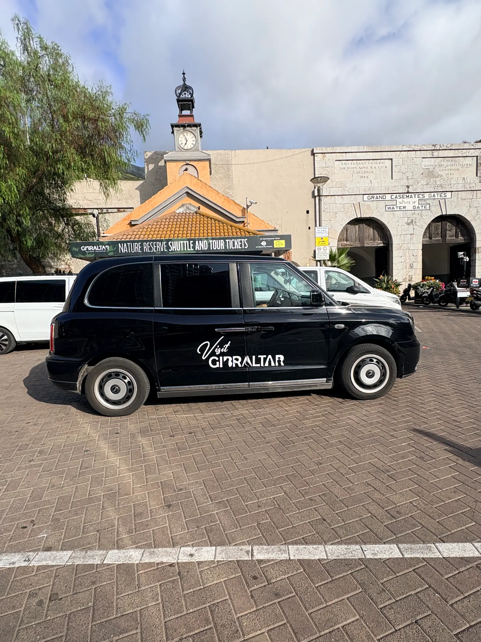 The Nature Reserve shuttle and tour ticket kiosk beside Grand Casemates Gates in Gibraltar, with a black Visit Gibraltar cab parked in front of it