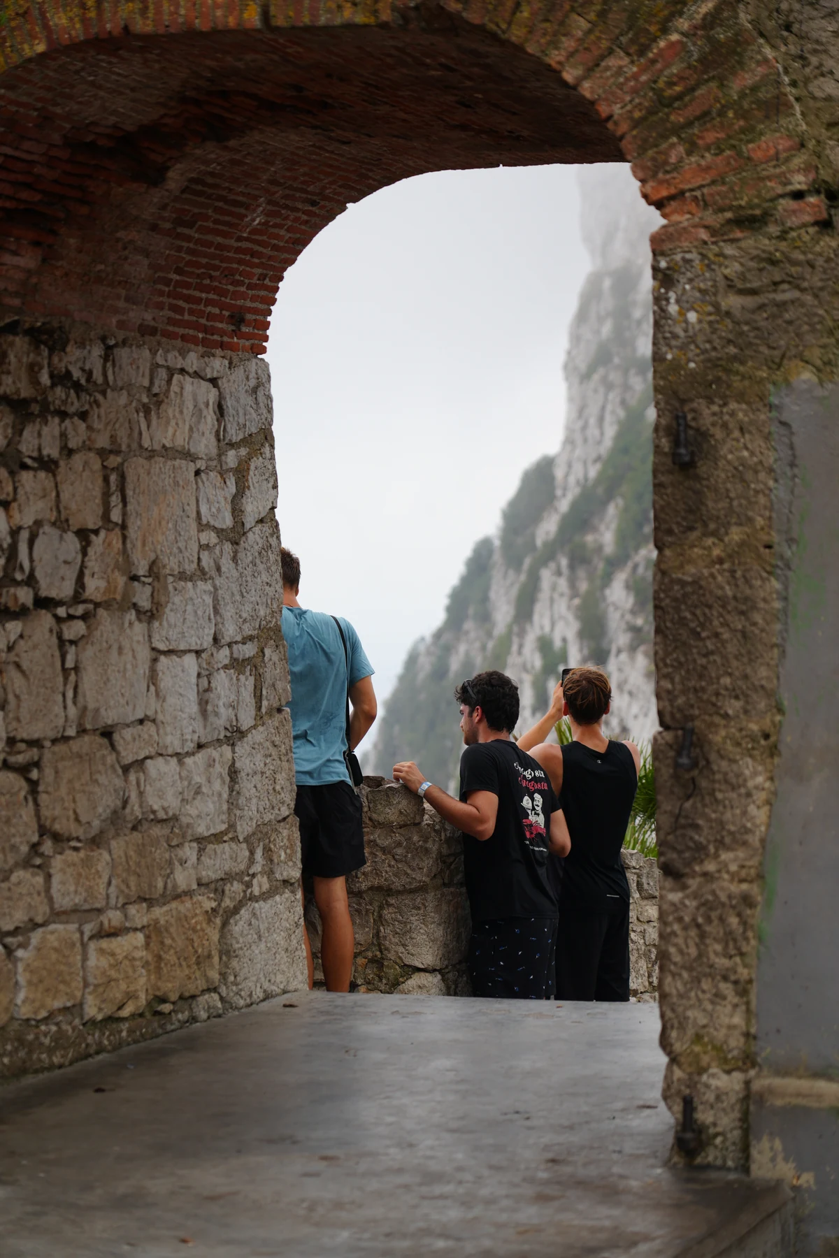 Visitors under a stone archway with misty cliffs behind, Gibraltar