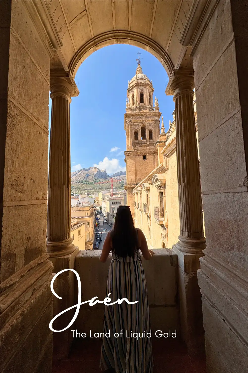 Woman looking through a stone archway towards Jaén Cathedral tower and the mountains beyond