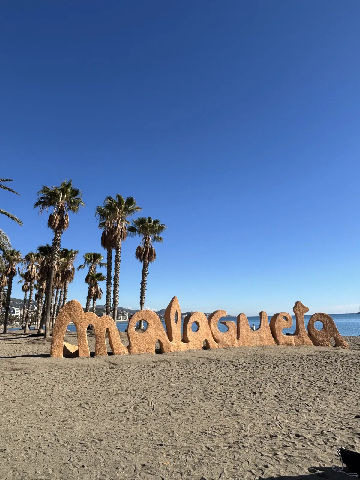 The Malagueta sign on a near-empty beach under a clear blue sky, with palm trees behind