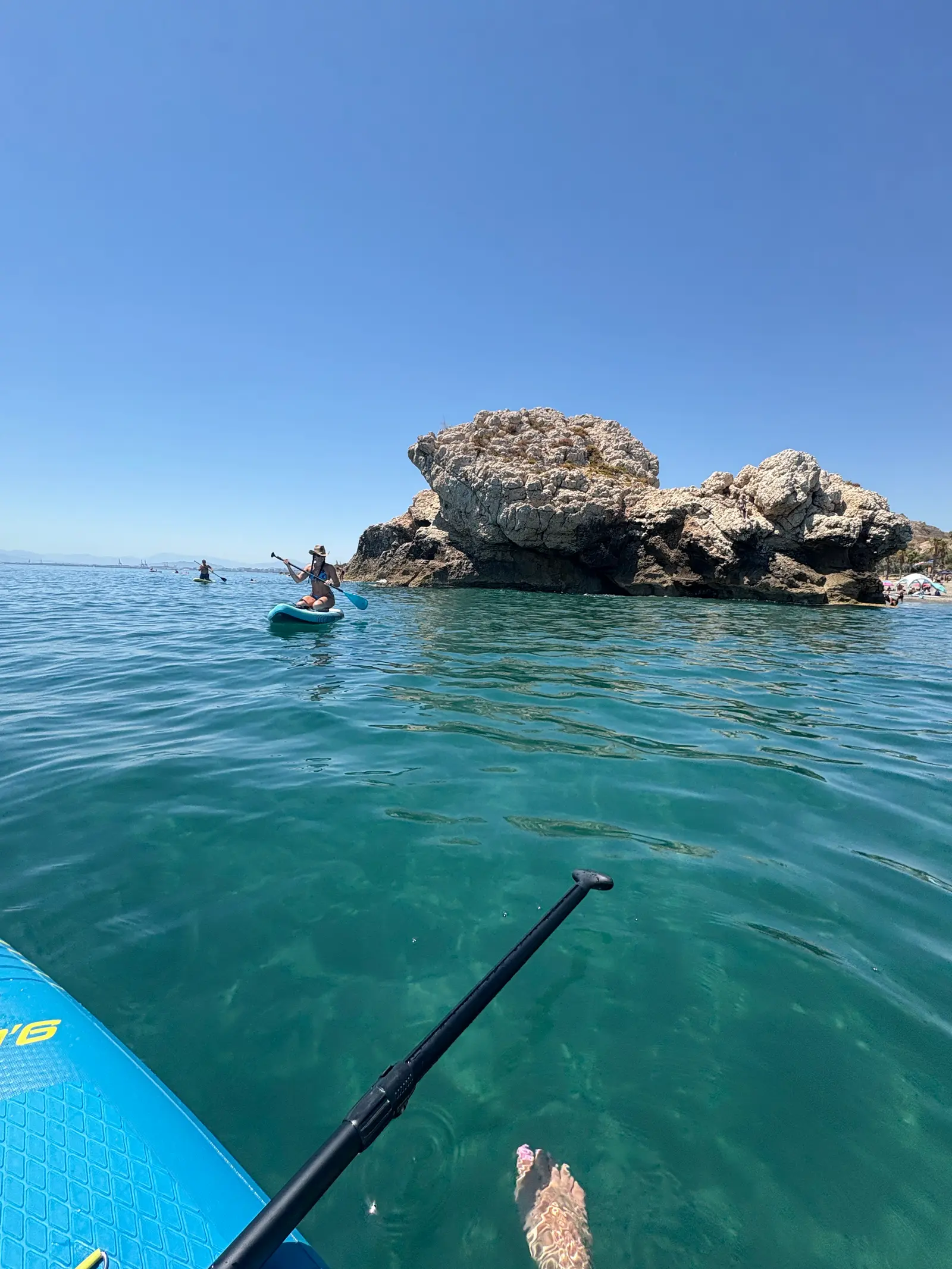 Paddleboarding past the Peñón del Cuervo sea rock in clear water