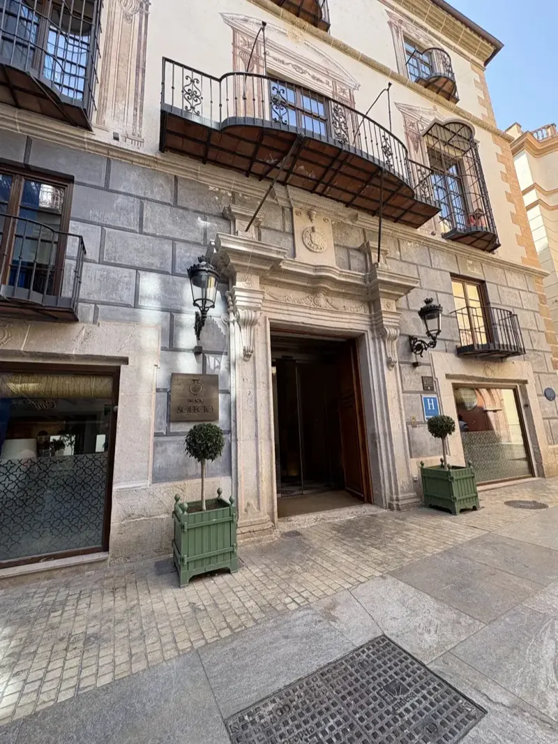 Palacio Solecio's carved stone entrance and wrought-iron balcony on a Malaga old town street, with the bronze Palacio Solecio sign by the door