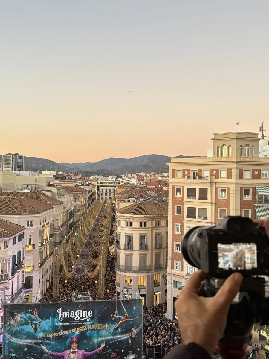 The Christmas lights along Calle Larios seen from a rooftop above the street, crowds filling the road below at sunset