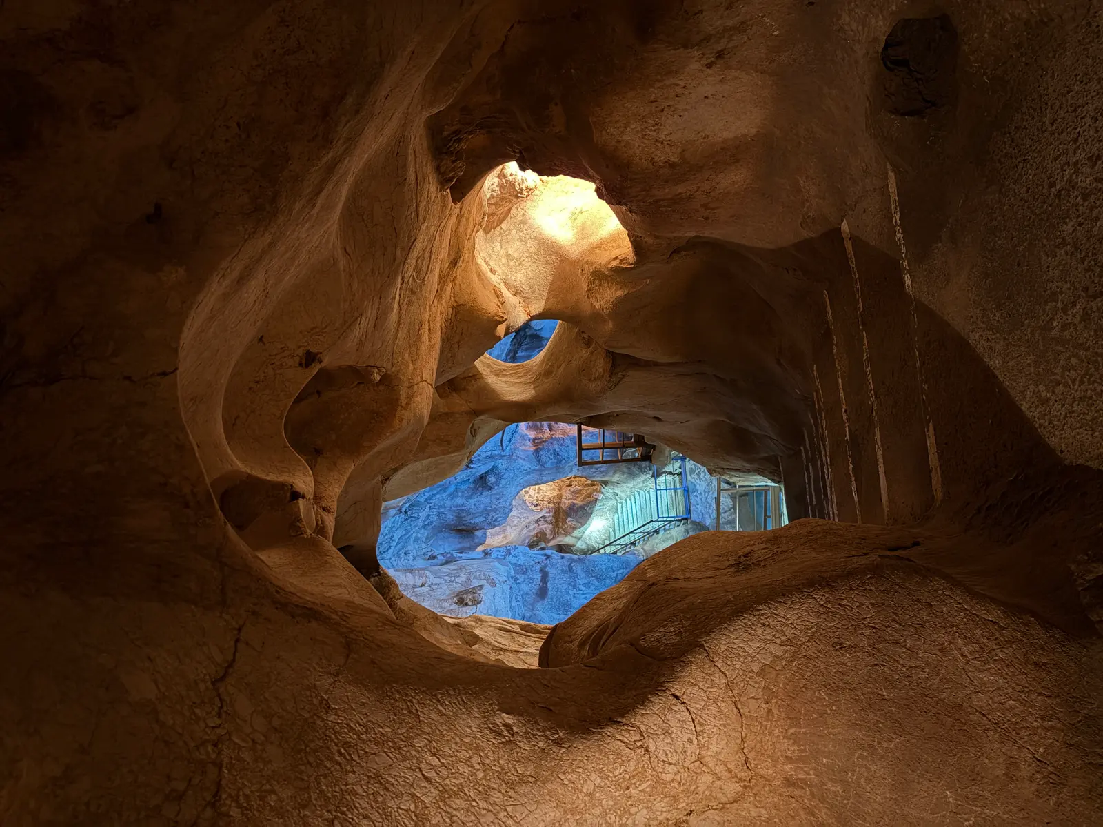 Natural window in the smooth eroded rock of the Cuevas del Tesoro framing a blue-lit chamber and staircase below