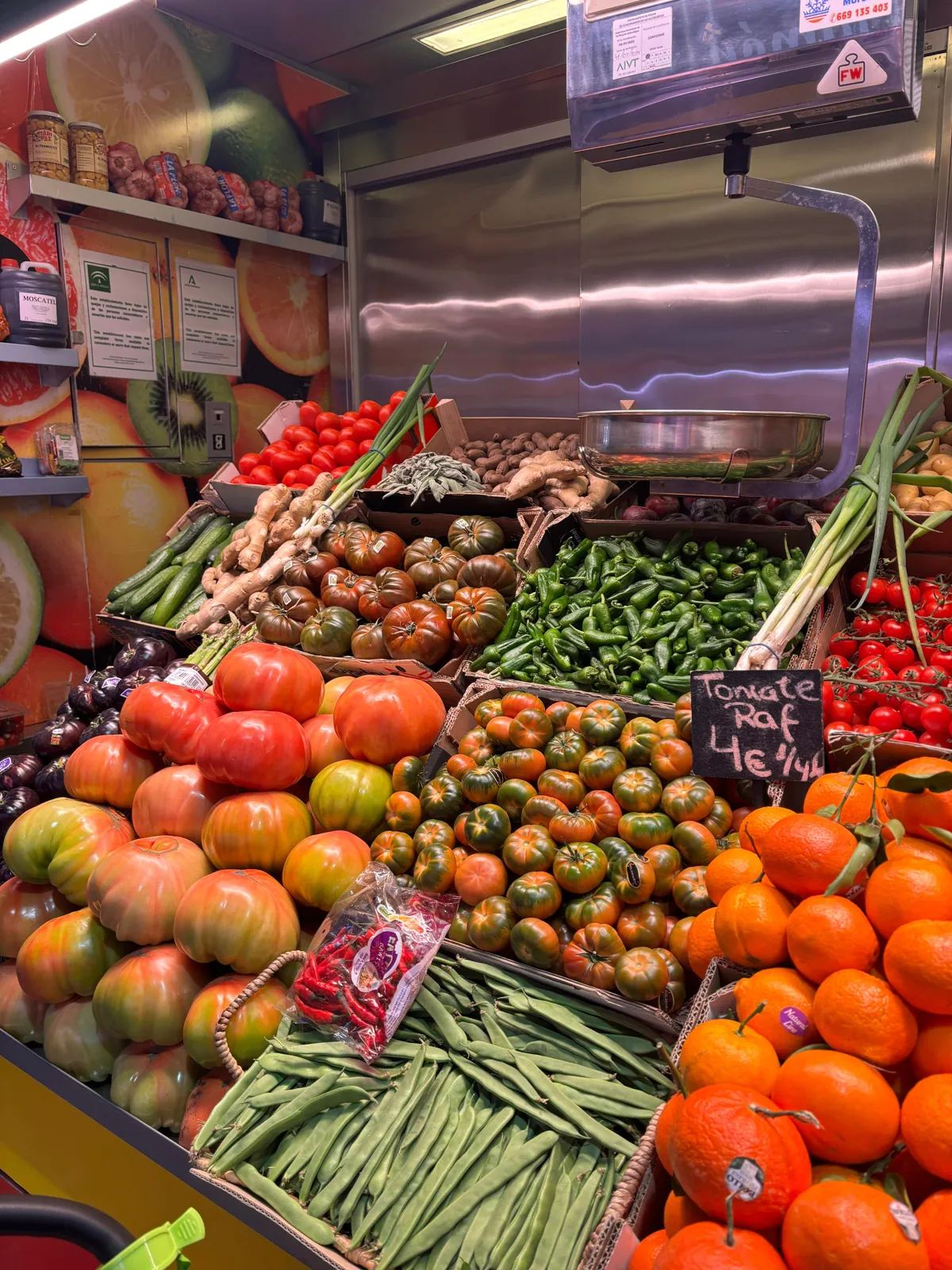 A fruit and veg stall at Malaga's Atarazanas market, piled with Raf tomatoes, oranges, green peppers and green beans