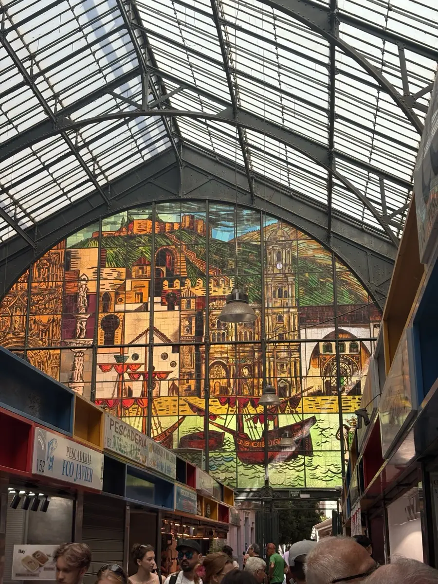 The arched stained-glass window inside Atarazanas Market in Malaga, showing sailing ships and the Alcazaba, above the Pescadería Fco Javier fish stall
