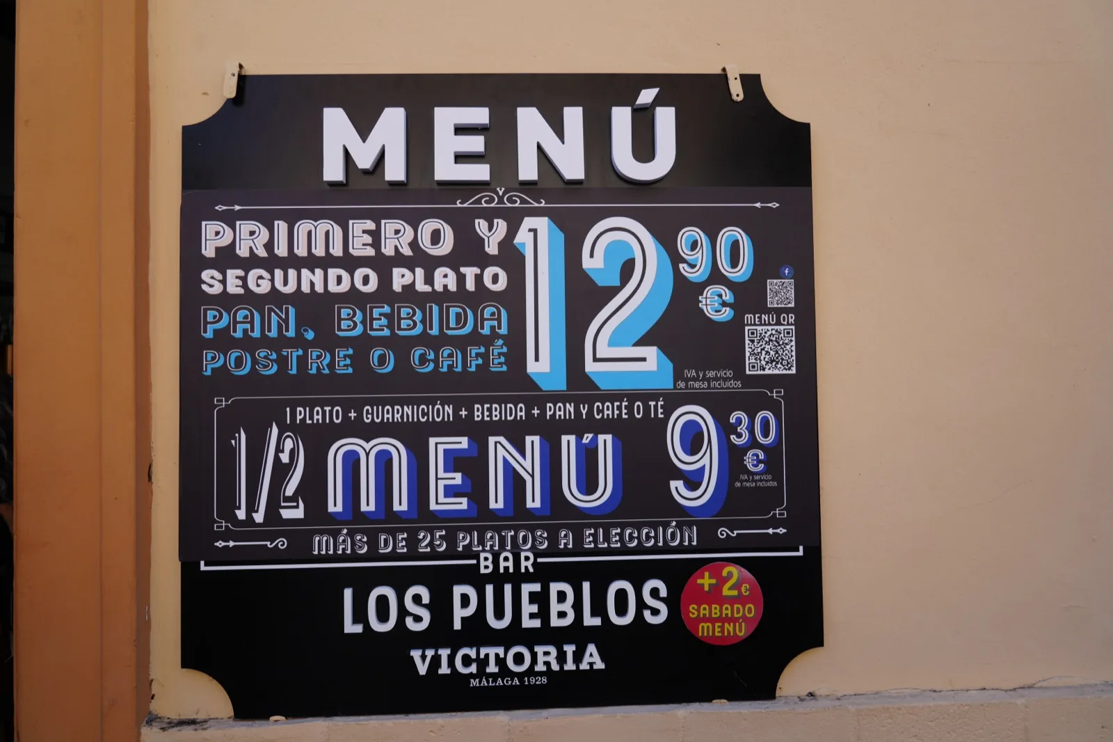 The Bar Los Pueblos menú del día board on Calle Atarazanas in Málaga, listing the full menu at €12.90 and a half menú at €9.30