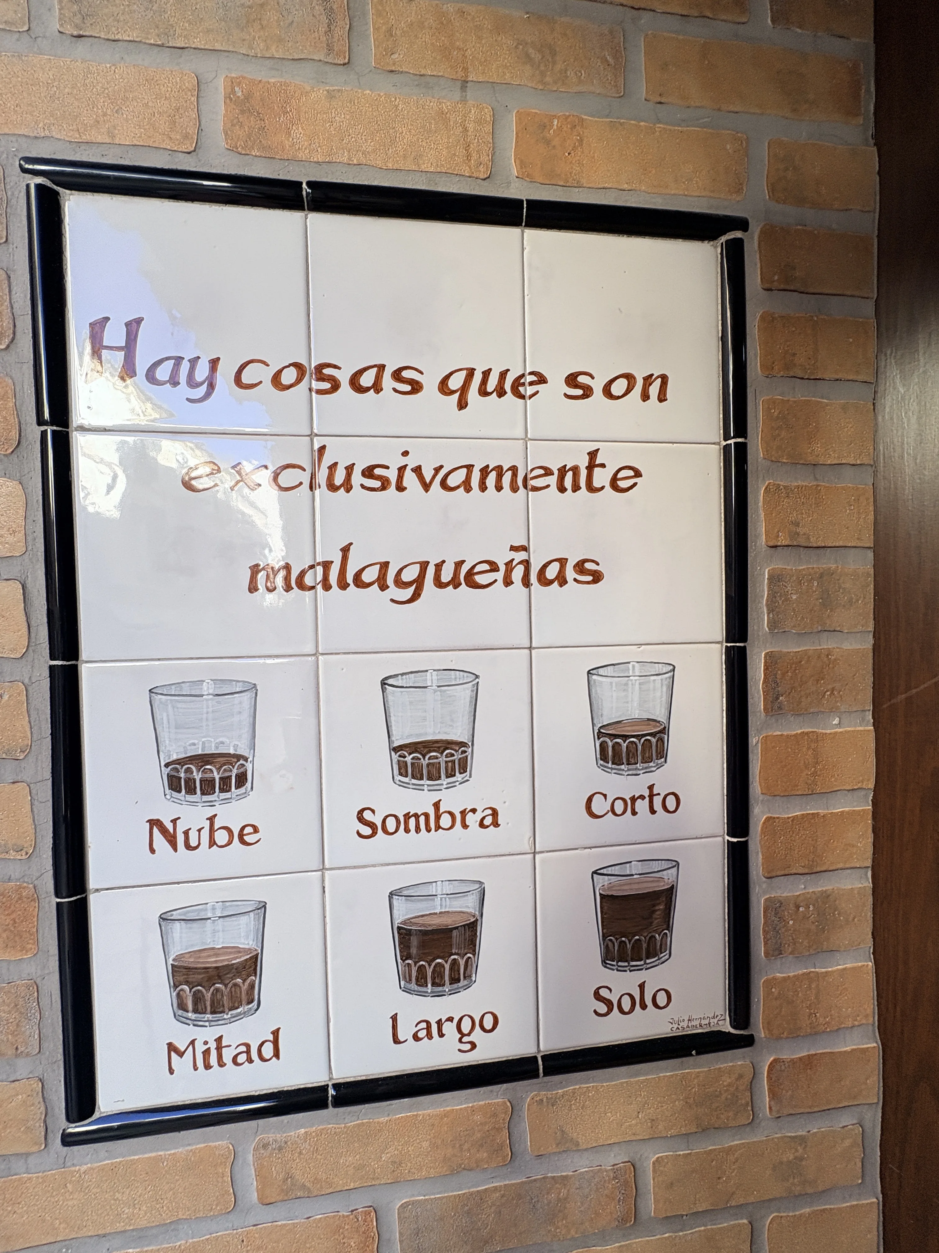 A tiled sign reading "Hay cosas que son exclusivamente malagueñas" at Bar Miguel in Málaga, showing six coffee glasses labelled nube, sombra, corto, mitad, largo and solo