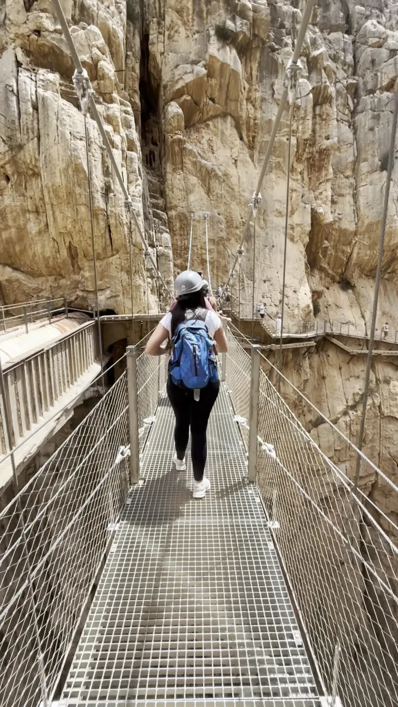 Heidi from behind crossing the Caminito del Rey suspension bridge between two cliff faces