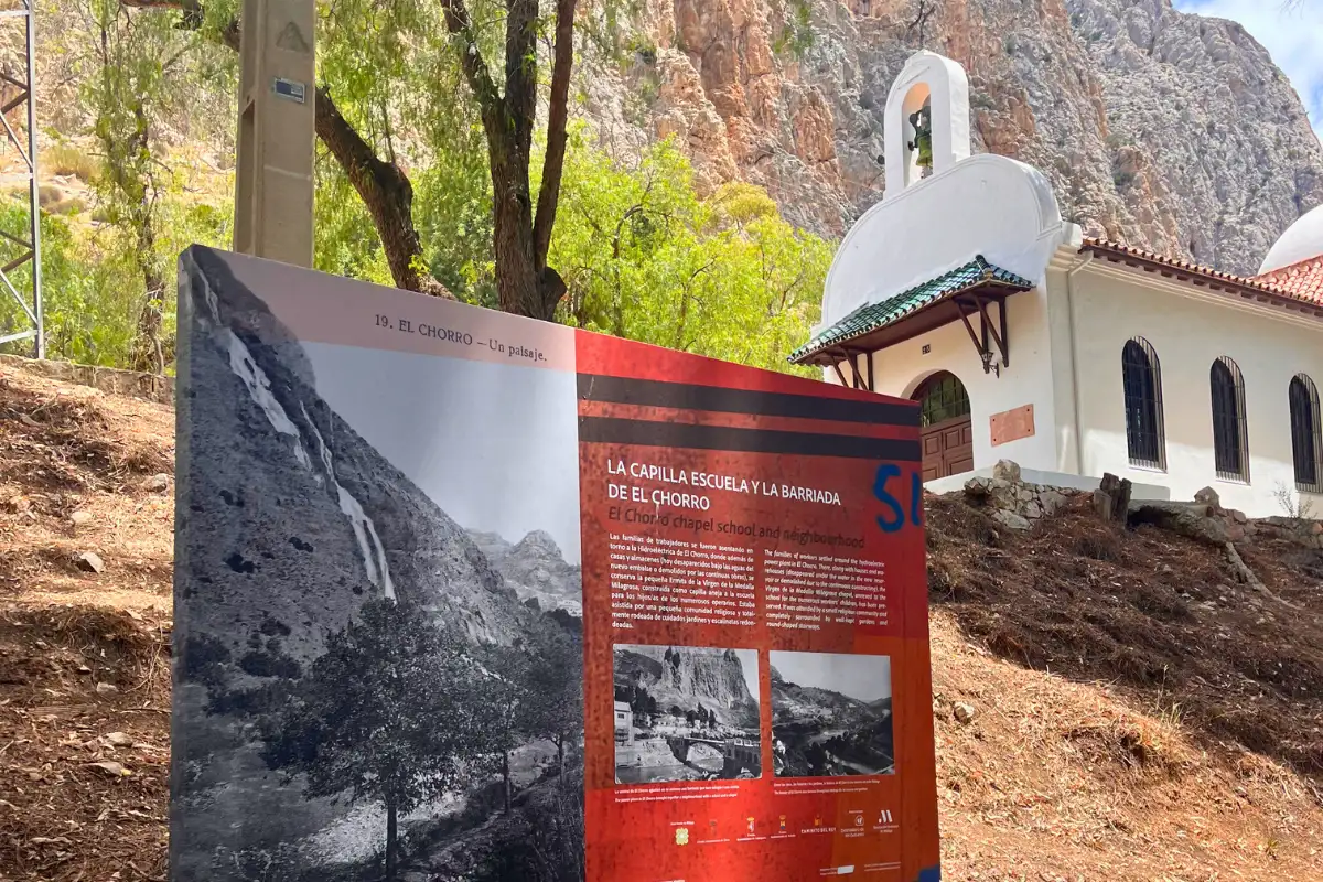 A sign depicting the Caminito del Rey original trail with the registration office behind it