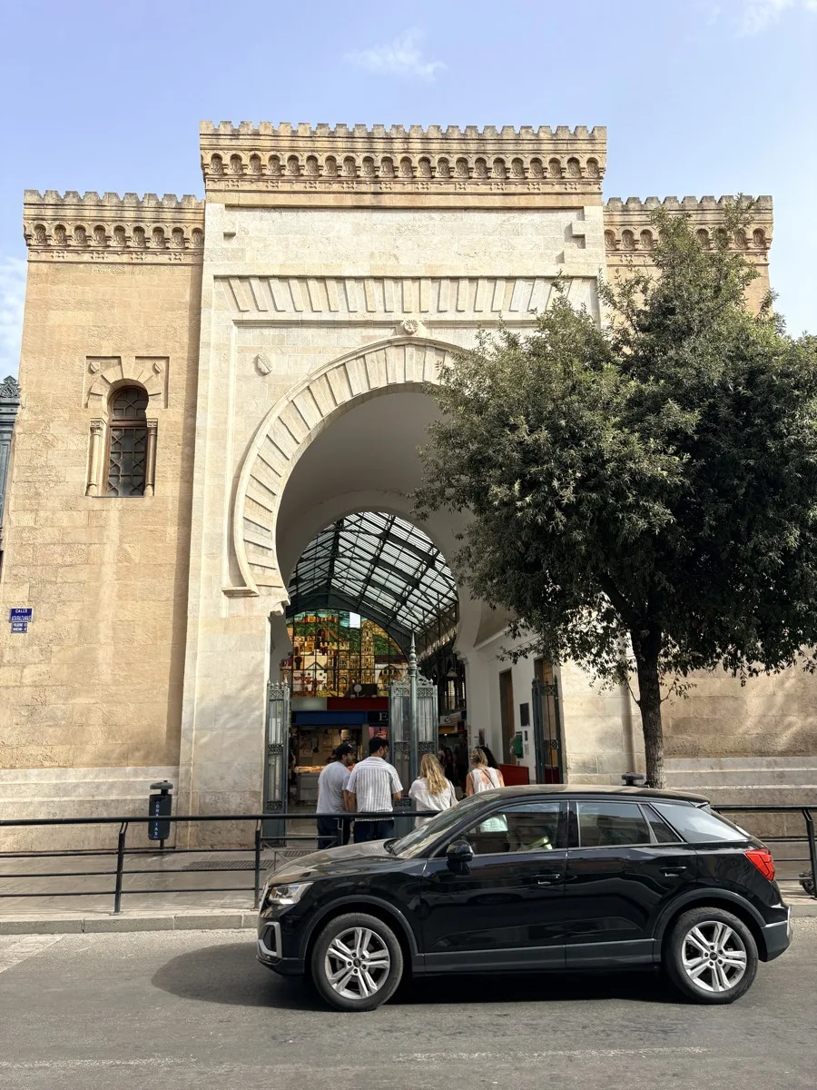 A black car parked on the street outside the stone arch of Atarazanas market in Málaga