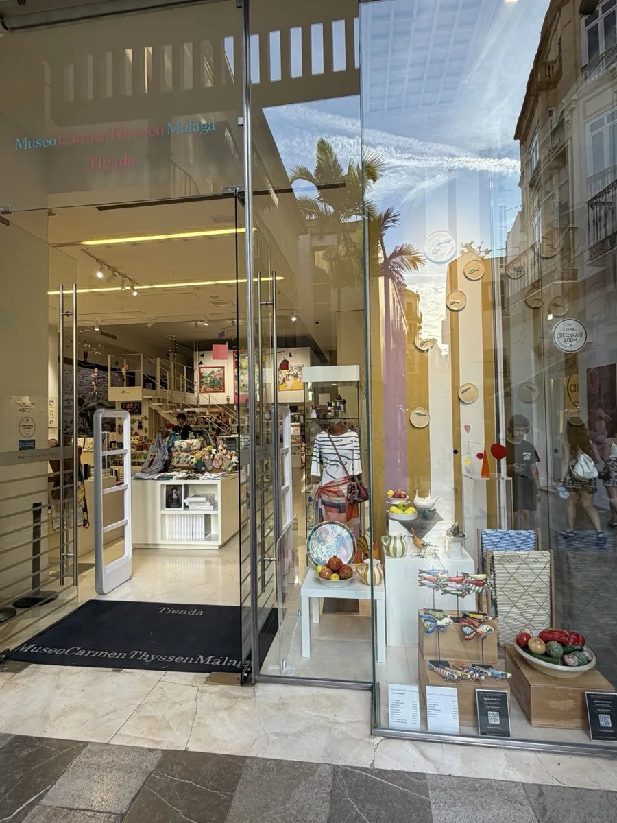 The Carmen Thyssen museum shop entrance in Malaga, glass doors opening onto a window display of ceramic plates, painted fish figurines and gift items