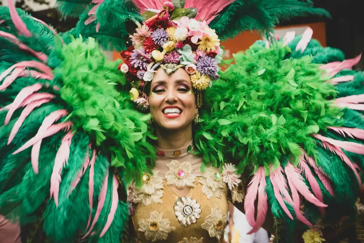 Carnival performer in elaborate green and pink feathered costume smiling at Málaga Carnival