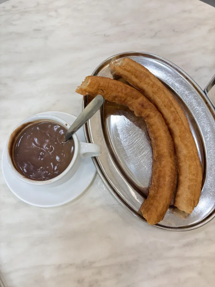 Two churros on a metal plate with a cup of thick hot chocolate at Casa Aranda in Málaga