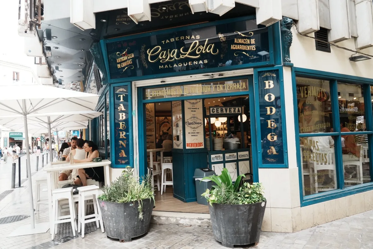 The blue-and-gold tiled frontage of Casa Lola on Calle Granada, white terrace tables under umbrellas and planters either side of the door